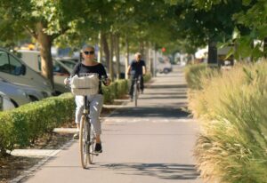 Ältere Frau die auf dem Radweg unter einer Baumallee mit einem Fahrrad fährt