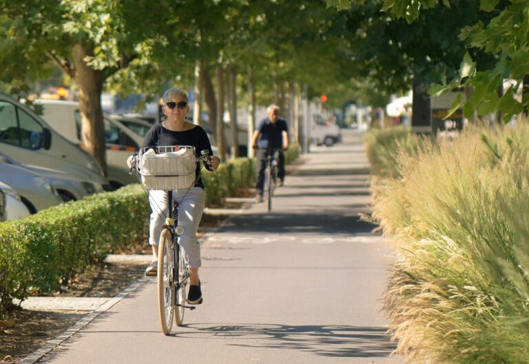 Ältere Frau die auf dem Radweg unter einer Baumallee mit einem Fahrrad fährt